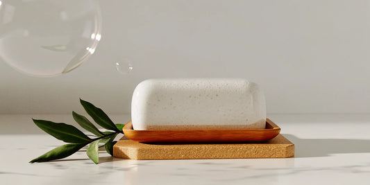 A bar of eco luxury hand soap with sustainable packaging on a wooden tray with green leaves.