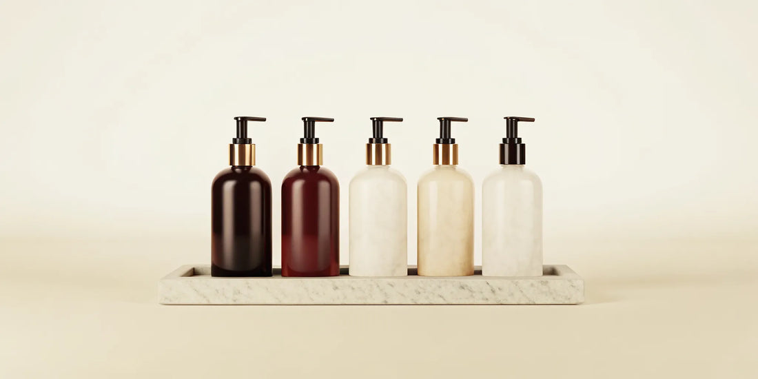 Five stylish liquid soap bottles with pumps on a marble tray in a chic bathroom.