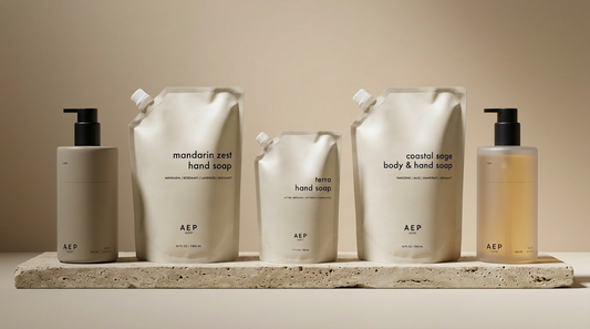 AEP Scent refill pouches and refillable bottles — Mandarin Zest, Terra and Coastal Sage lined up on a travertine ledge