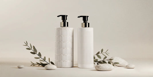 A beautifully styled bathroom counter with minimalist translucent soap dispensers, eucalyptus leaves, and natural stone decor in soft natural lighting