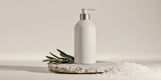 Sleek ceramic bottle of non-toxic body wash on marble surface with sage and sea salt accents
