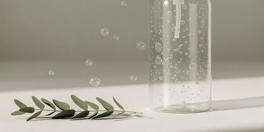 Eucalyptus hand soap refill in a clear bottle next to a fresh eucalyptus branch.