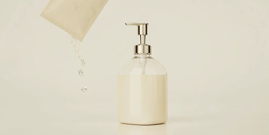 A hand pouring a hand wash refill pack into a soap dispenser.