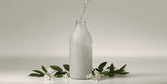 A glass bottle being filled with a natural body wash refill, surrounded by fresh botanicals.