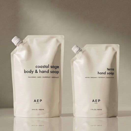 Two AEP hand soap containers, one labeled 'mandarin zest' and the other 'terra', on a reflective surface with a neutral background. 