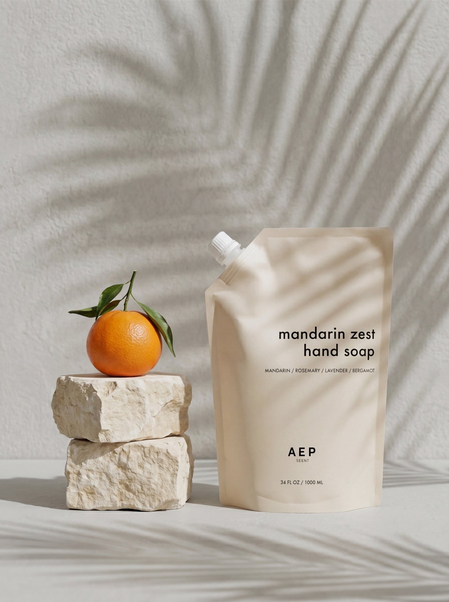 mandarin zest pouch next to a crisp fresh mandarin laid on top of 2 pieces of decor rock. clean background with palm tree shadow